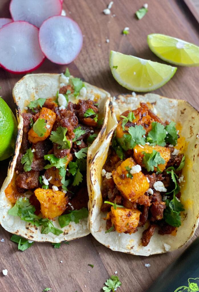 al pastor tacos with pineapple and cilantro on a wooden board