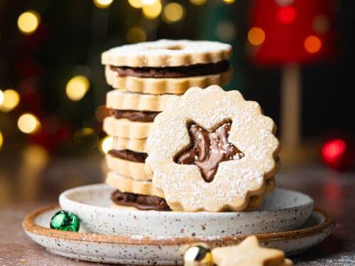 Espresso shortbread cookies stacked on a white plate with coffee beans and a steaming mug of coffee in the background, warm natural light