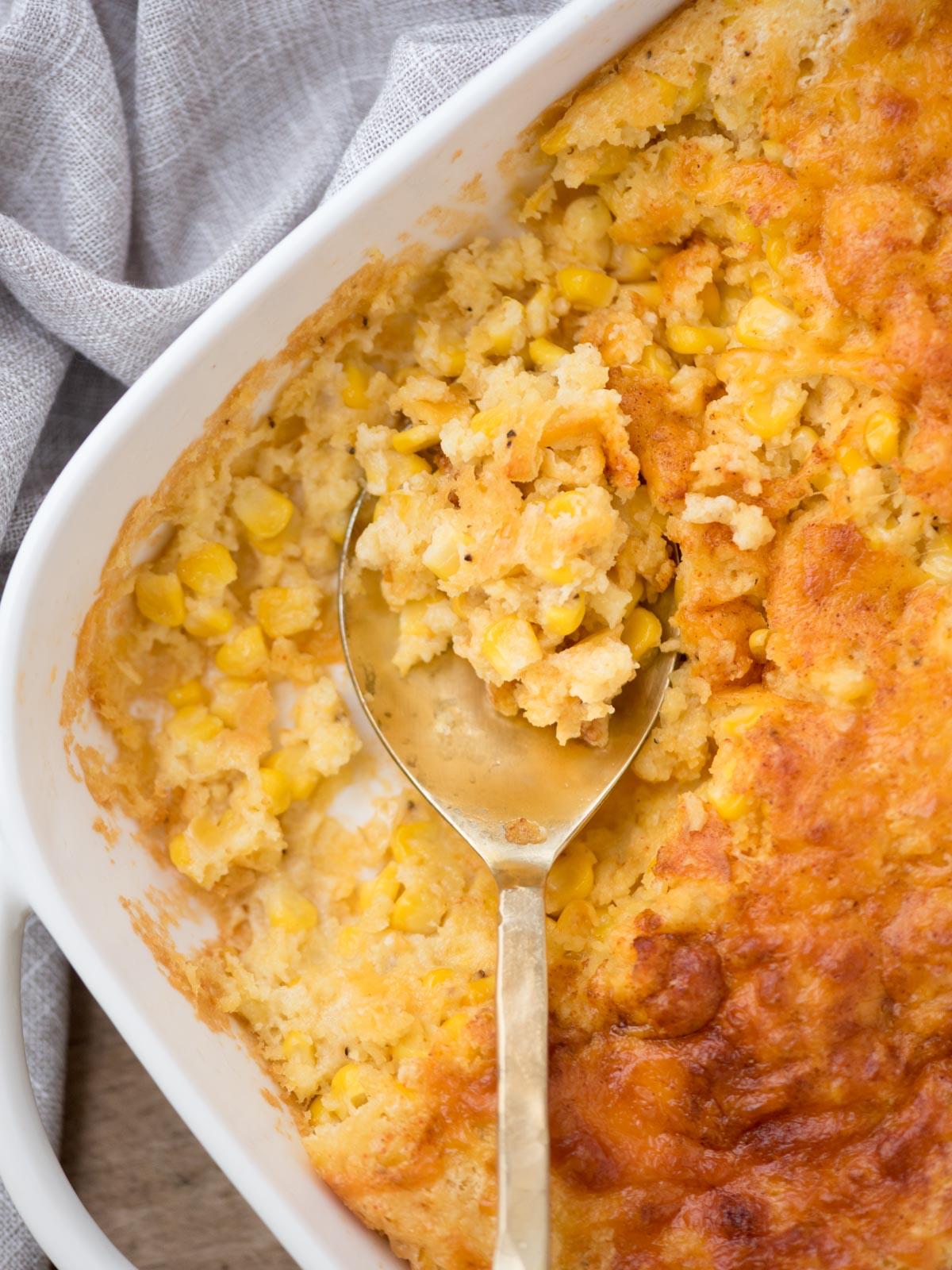 Close-up of baked corn casserole being scooped, showing creamy texture and golden top