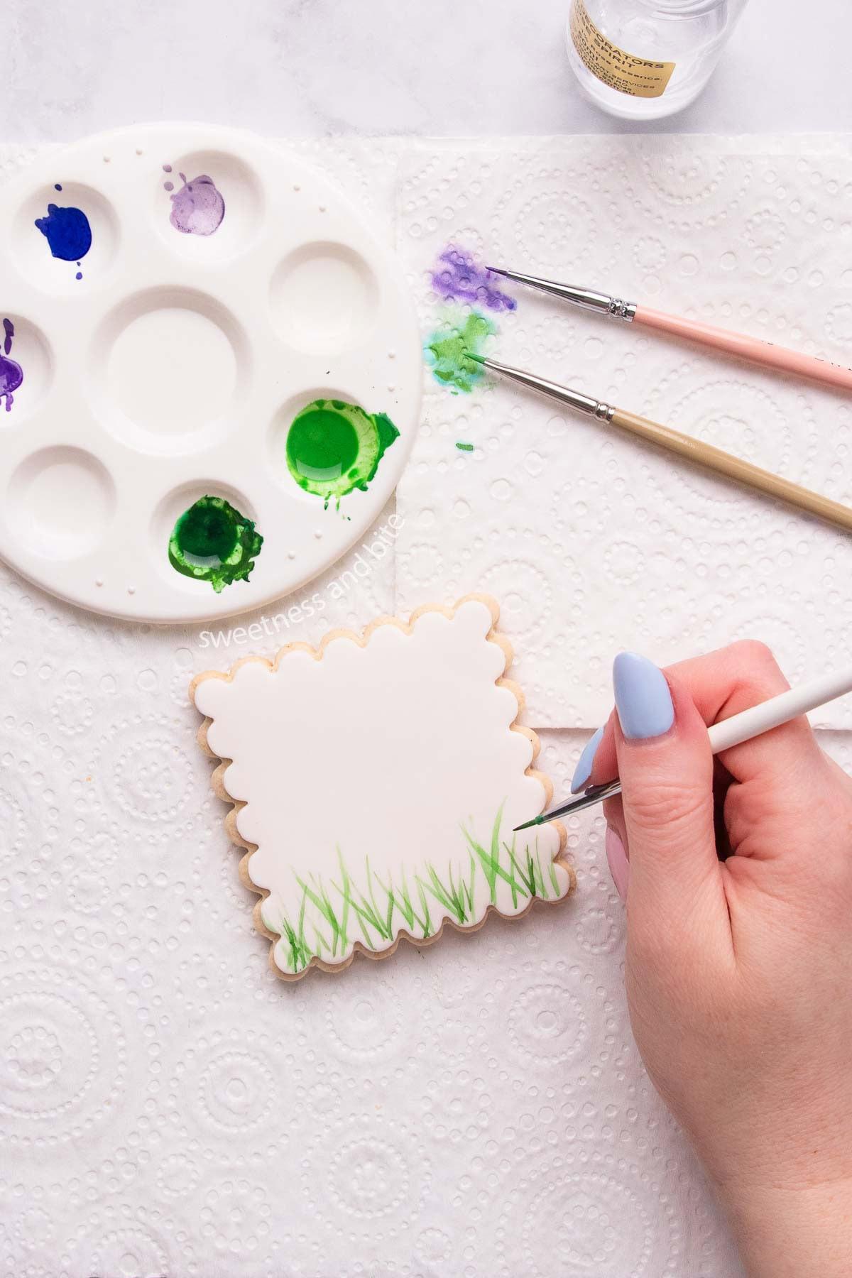 Person hand-painting a butter cookie with a fine brush, close-up of colorful edible paints and palette
