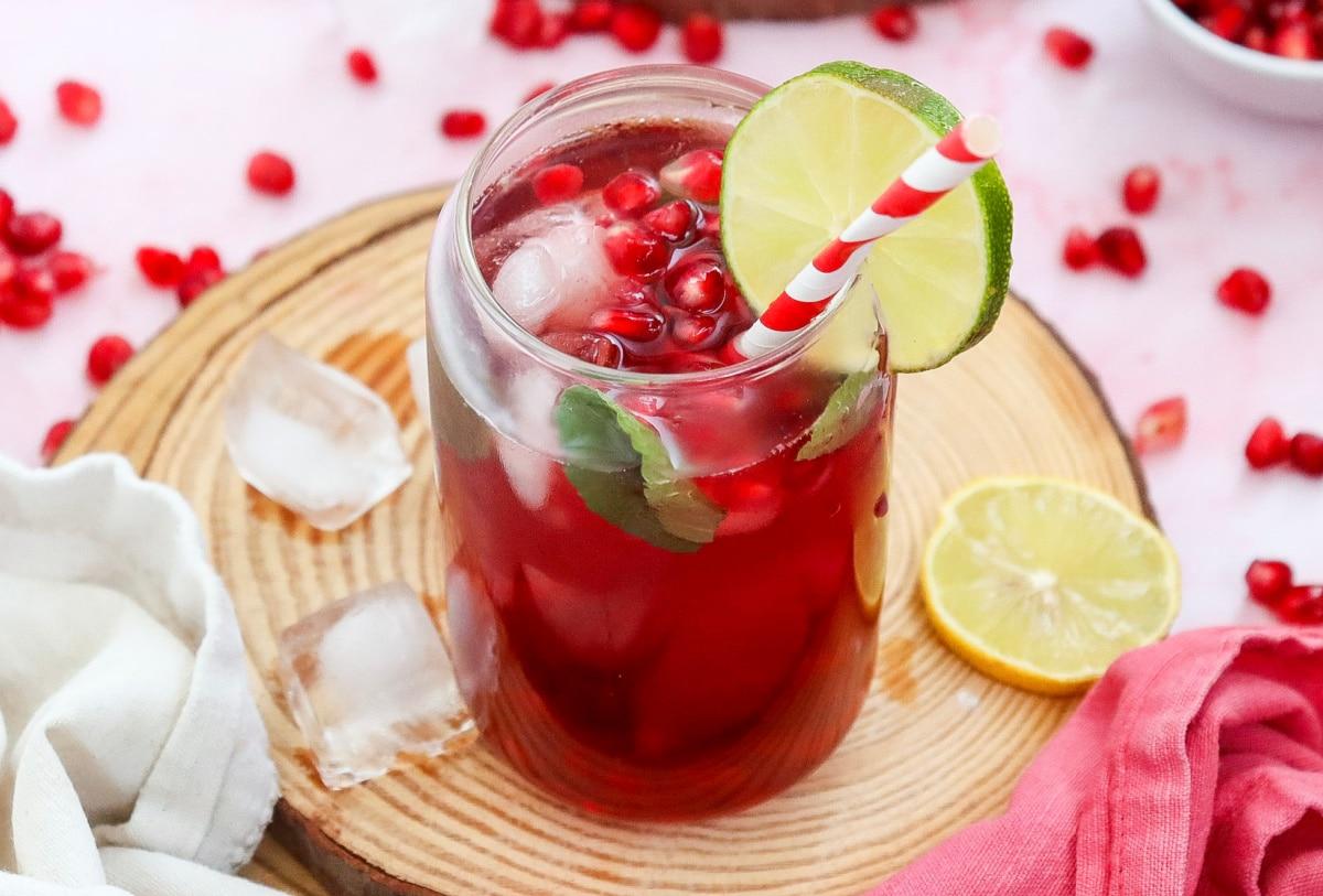 close-up of a hand garnishing a pomegranate mocktail with a lime slice and mint sprig