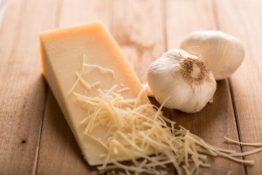 fresh garlic cloves and a wedge of Parmesan cheese on a rustic wooden board