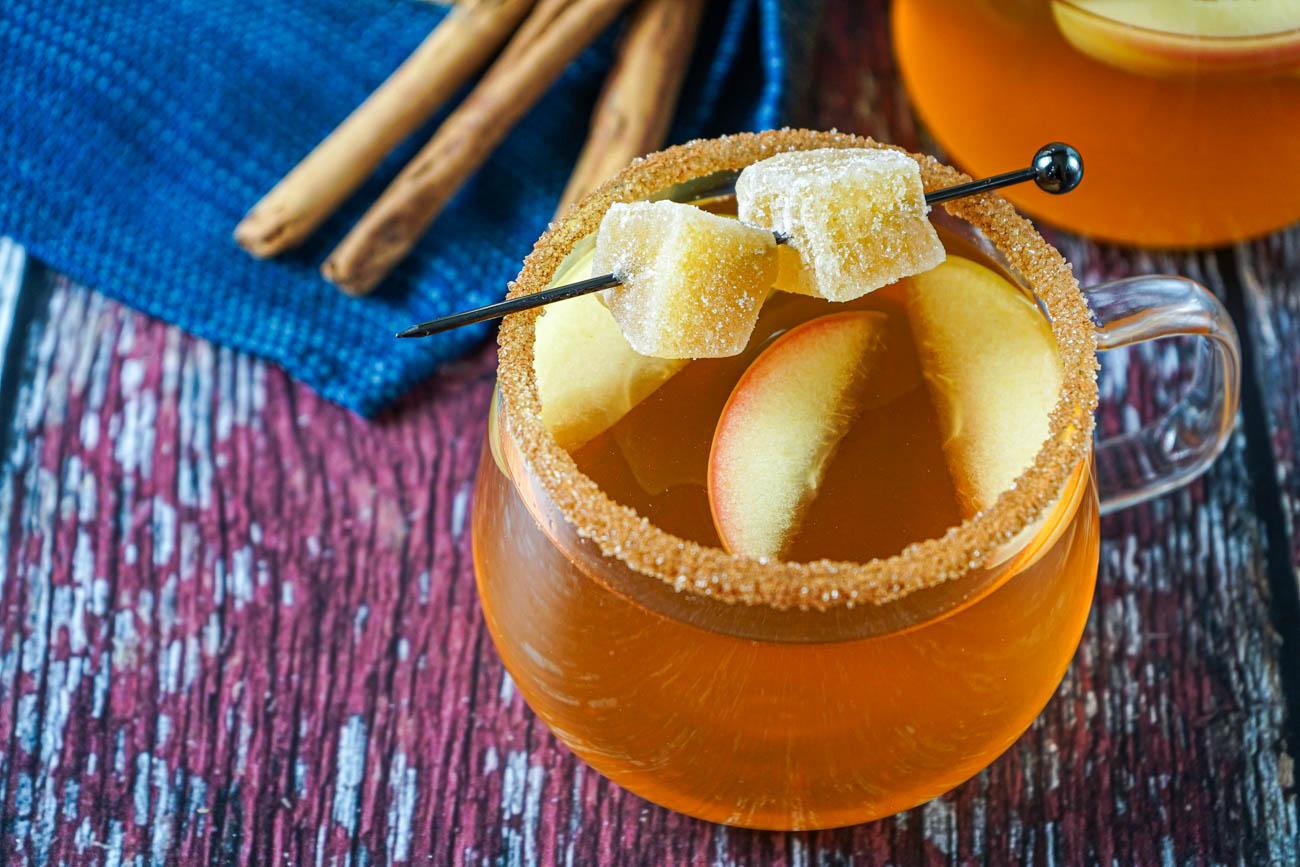 Close-up of a rustic pitcher of apple spice punch garnished with apple slices and cinnamon sticks