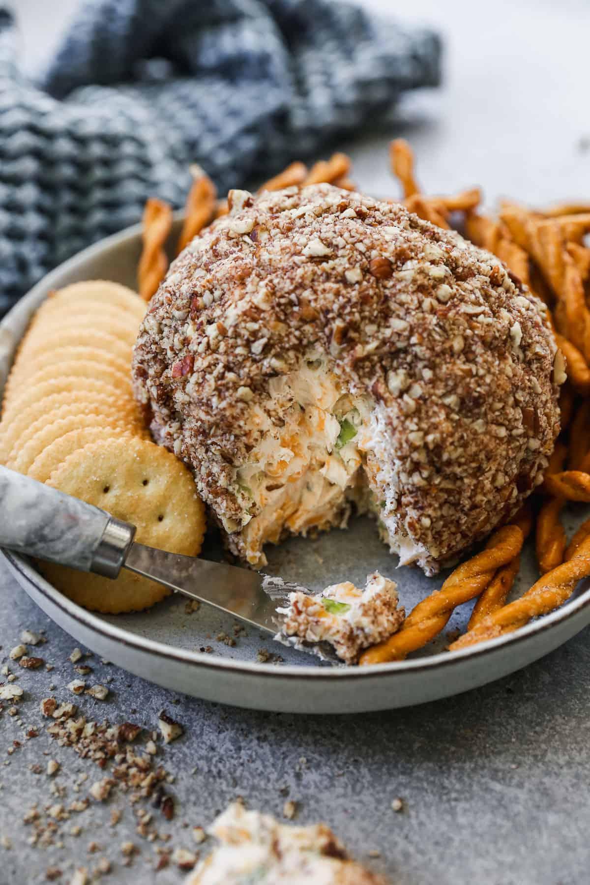 Hands pressing a mixture of chopped nuts onto a formed cheese ball, showing good coverage.