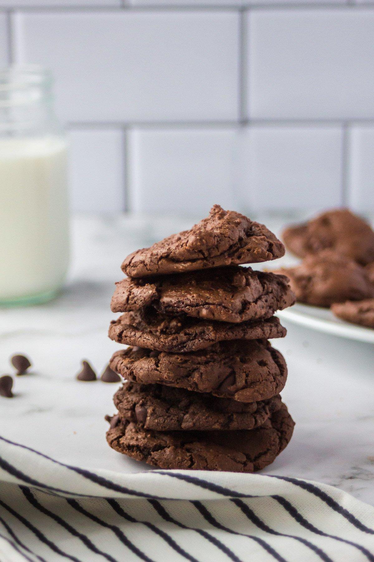 Warm double chocolate cookies stacked on a cooling rack, gooey chocolate chips visible, next to a glass of milk