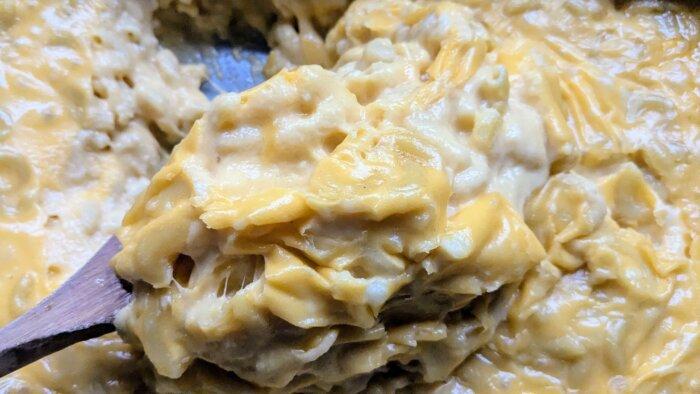 serving spoon scooping a portion of cream-top mac and cheese from a baking dish