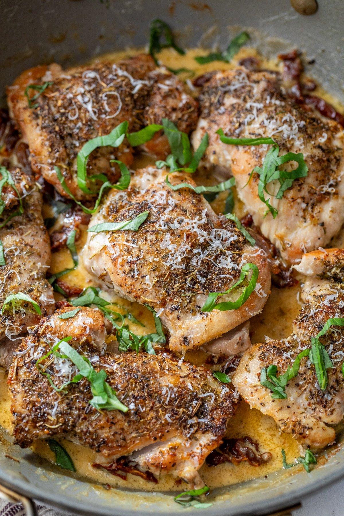Close-up of golden brown chicken pieces searing in a large skillet with sun-dried tomatoes and garlic