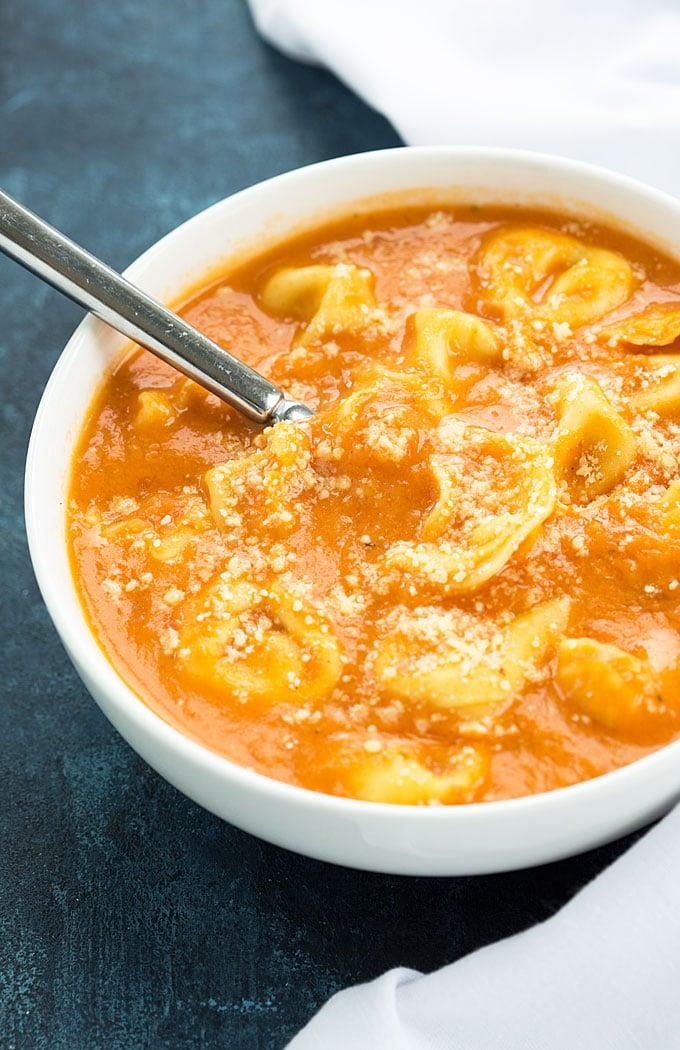 close-up shot of creamy tomato tortellini soup being poured into a bowl