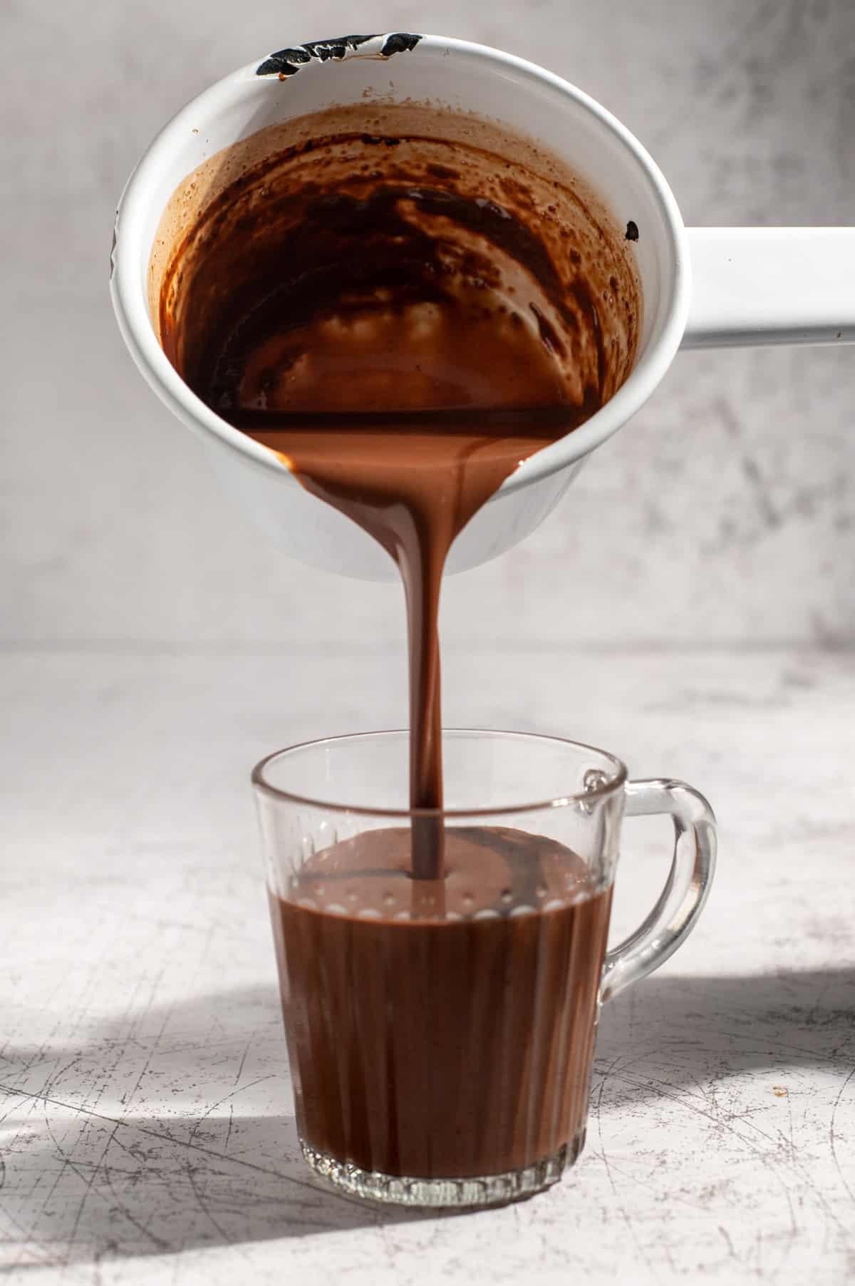 Close-up of thick, dark molten chocolate dripping into a mug of hot milk