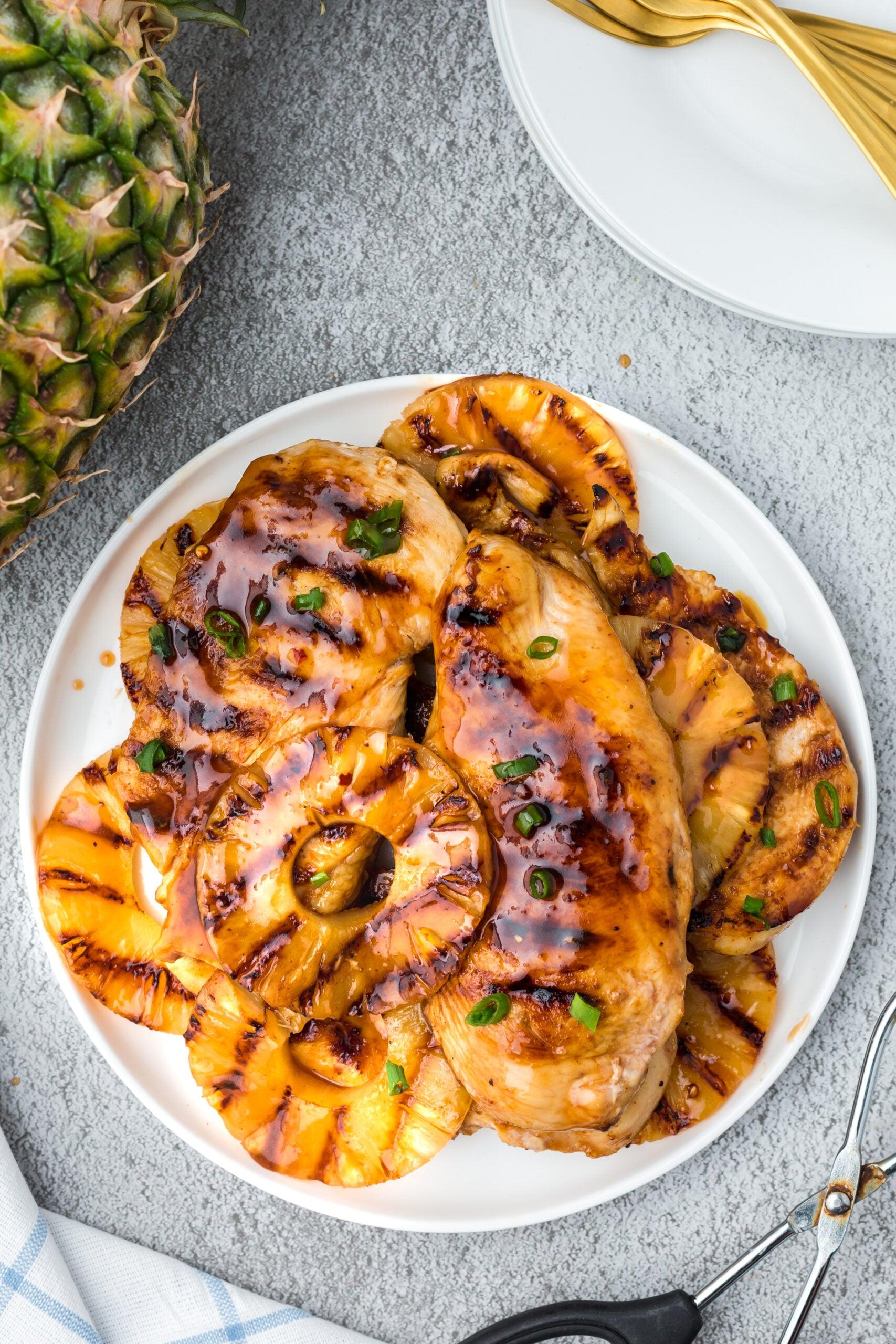 person grilling marinated chicken alongside pineapple slices on a barbecue