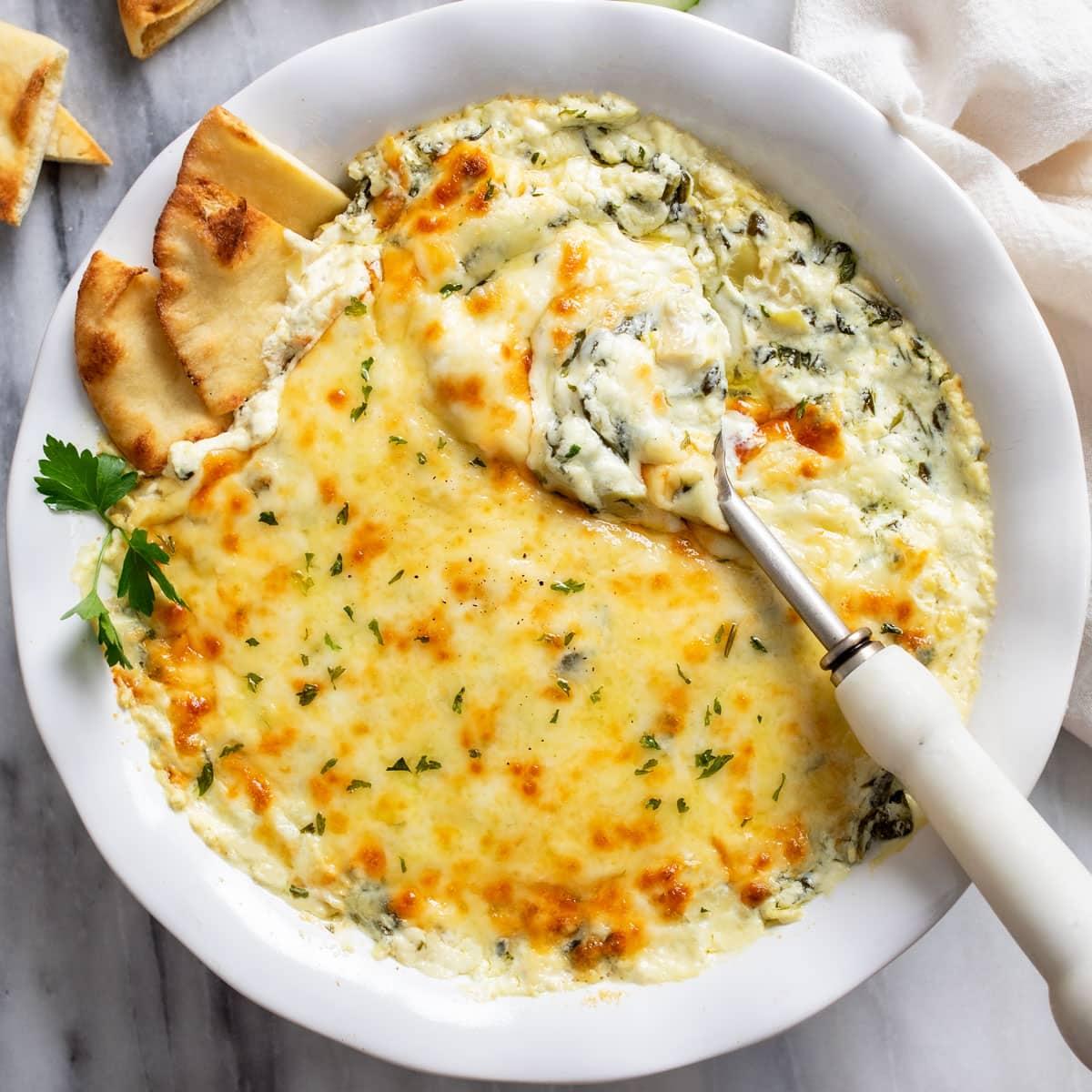 Cozy scene with a warm spinach artichoke dip, a blanket, and friends sharing a moment
