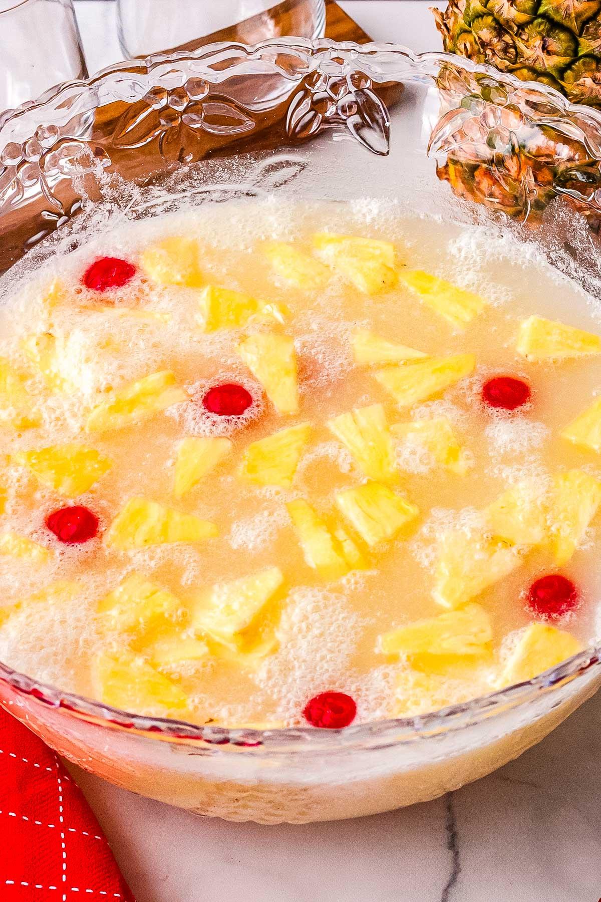 Bright yellow pineapple punch in a clear punch bowl with slices of lime and pineapple