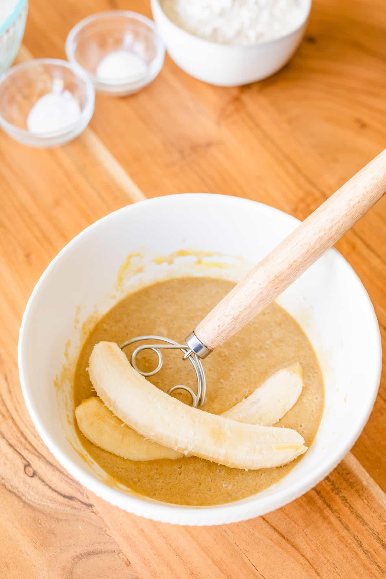 Hands gently mixing banana bread batter in a ceramic bowl, light coming from window