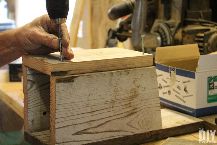 hands assembling a birdhouse with screws and wood
