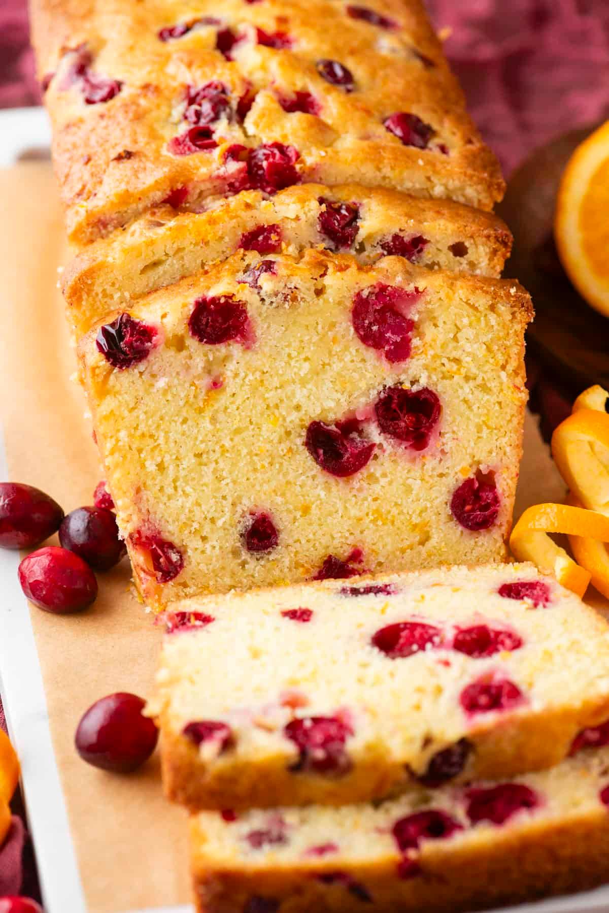 close up of a slice of cranberry orange bread showing cranberries and orange zest, steam gently rising