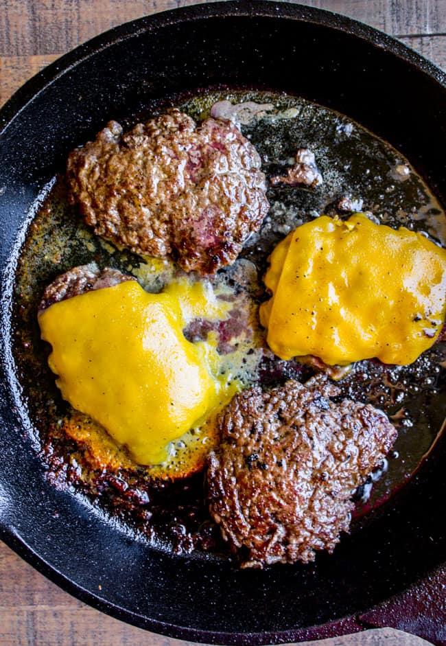 Homemade smash burgers cooking on a cast iron griddle with steam rising