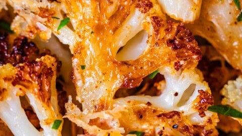 Close-up of golden-brown roasted cauliflower florets with crispy edges, garnished with fresh parsley