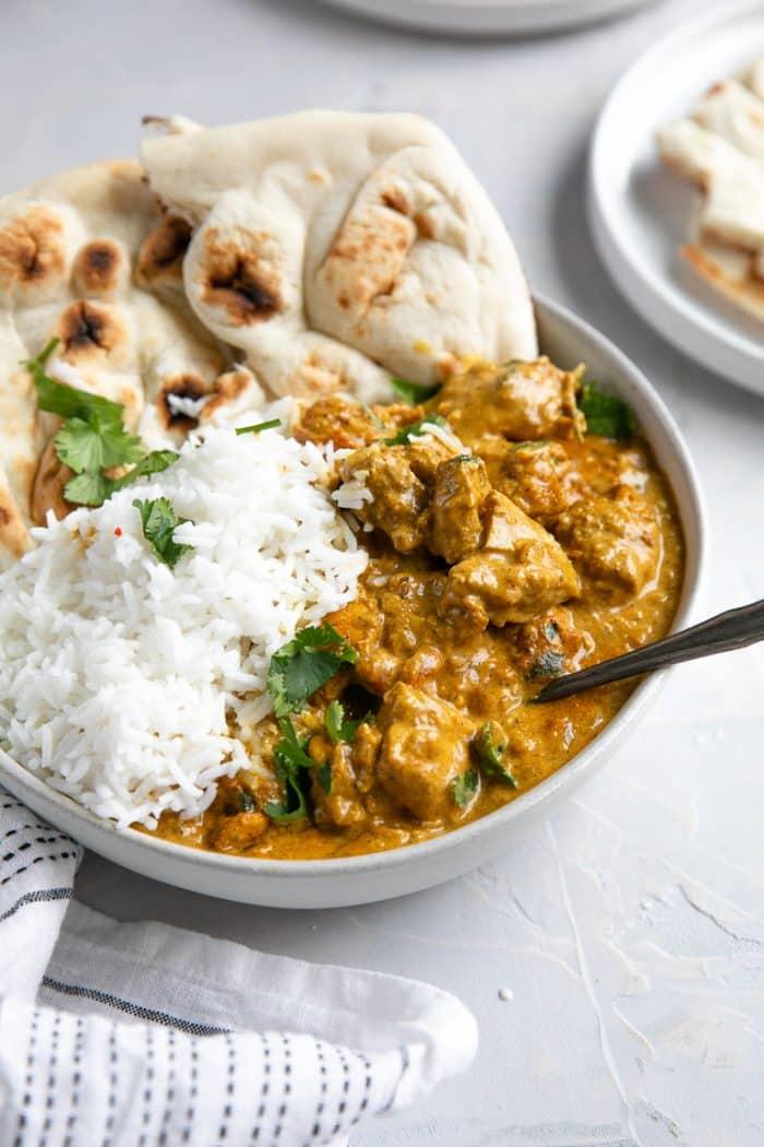 Butter chicken served in a rustic bowl with fluffy rice and torn naan bread, ready to eat