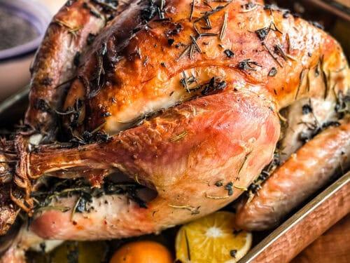 beautifully roasted whole turkey with crispy, dark golden skin, pepper rub visible, garnished with fresh herbs, on a festive holiday table