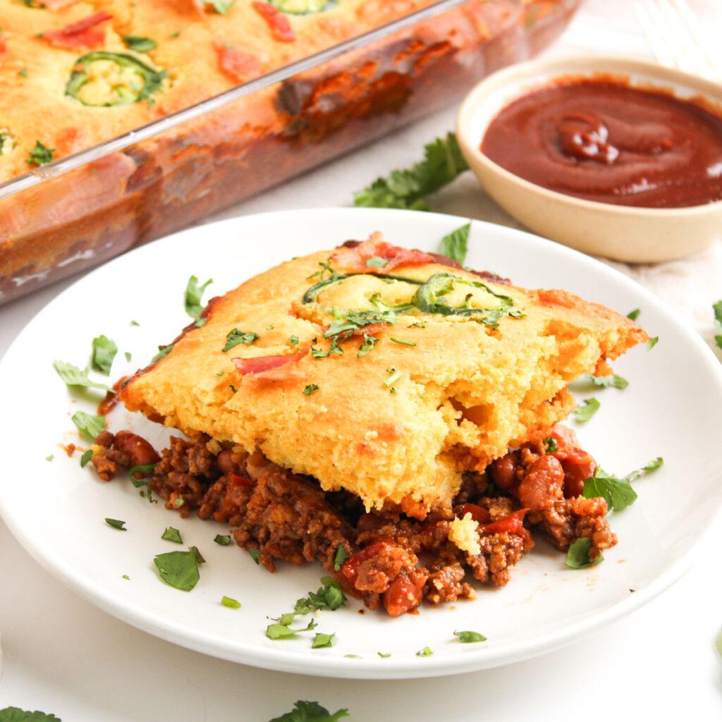 Ingredients for Cowboy Casserole laid out on a wooden cutting board: ground beef, corn kernels, shredded cheddar cheese, potatoes, onions, garlic