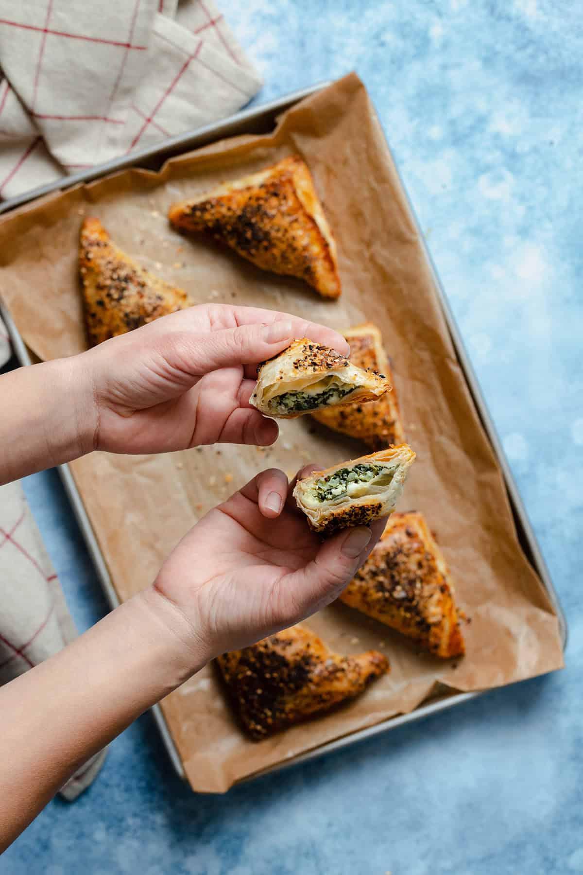 Hands holding a freshly baked spinach feta pastry triangle, steam rising
