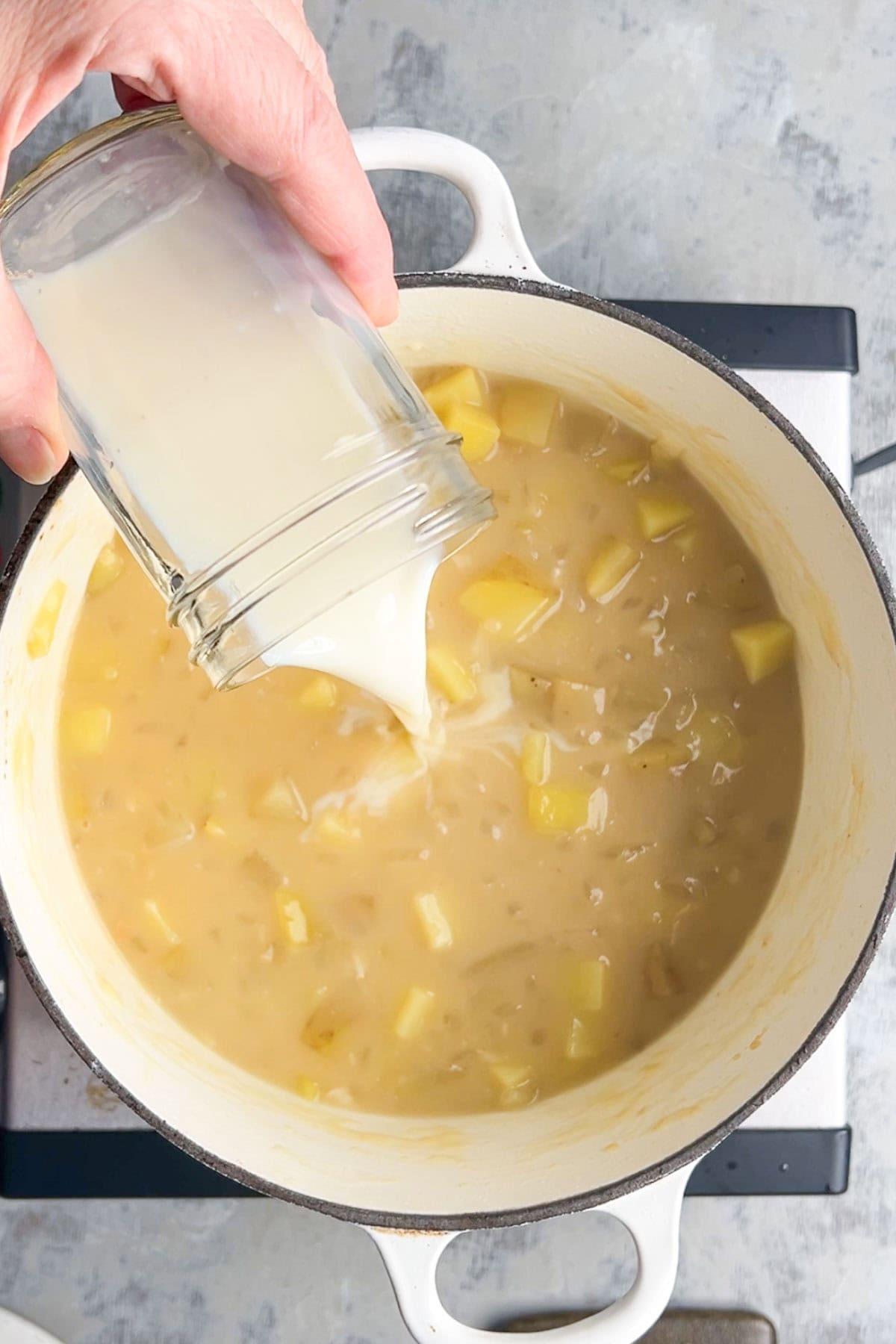 Hand stirring a pot of creamy potato soup on a stovetop