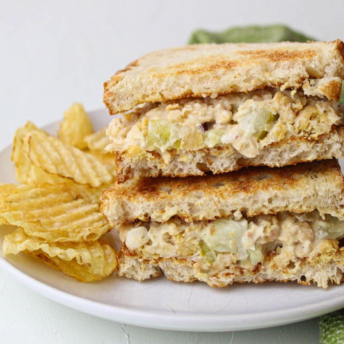 two chickpea salad sandwiches cut in half, arranged on a plate with a side of pickles
