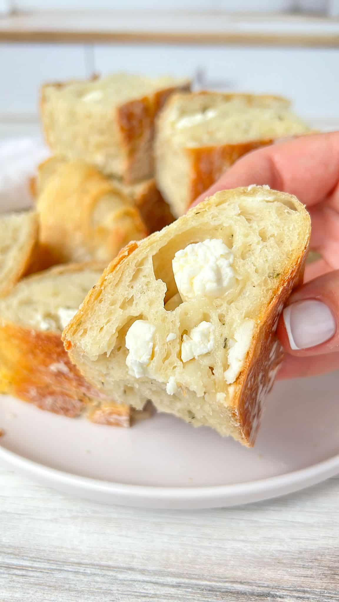 Hands scooping warm baked feta with a crusty bread