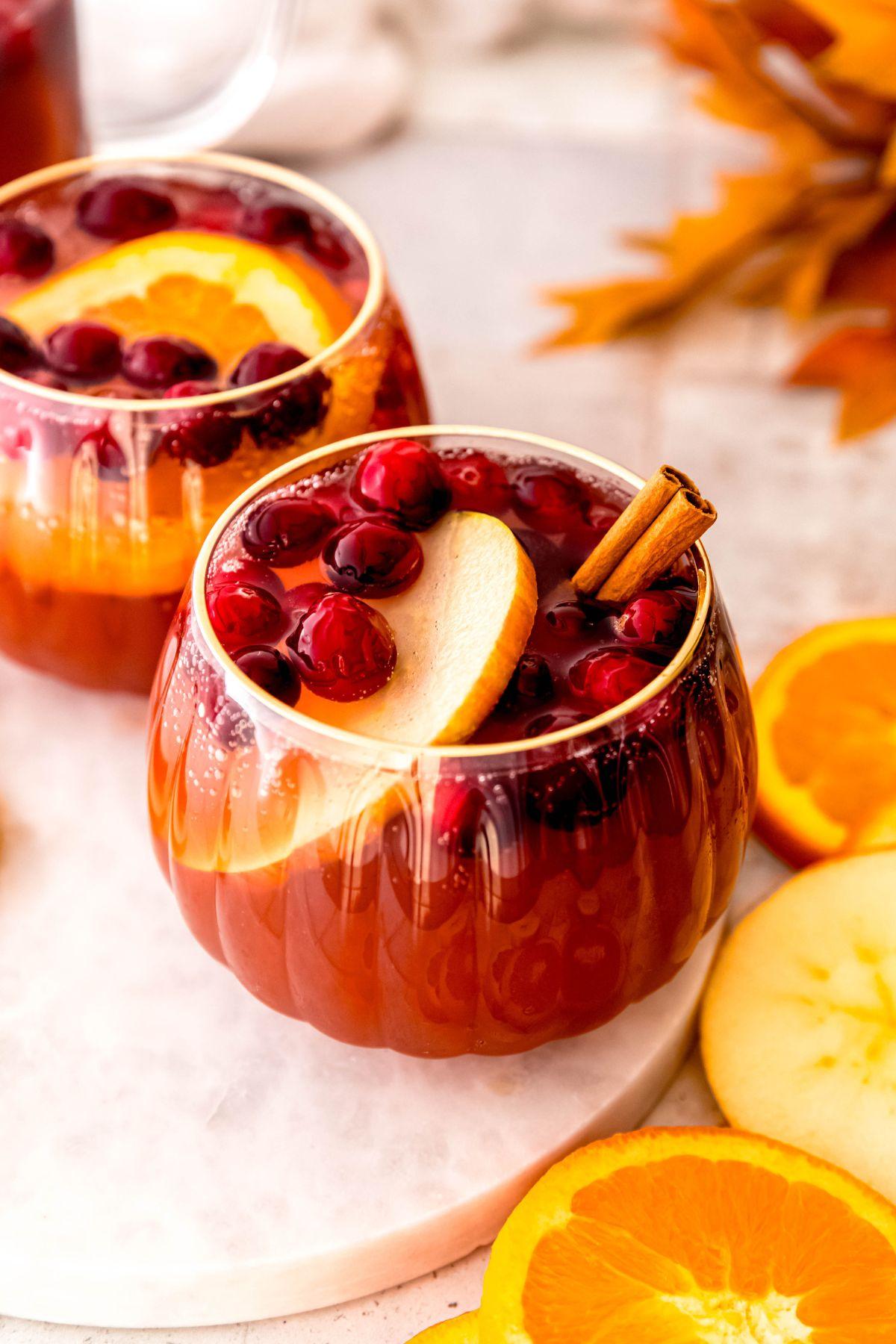 Vibrant orange clove punch steaming in a clear glass pitcher on a festively decorated table