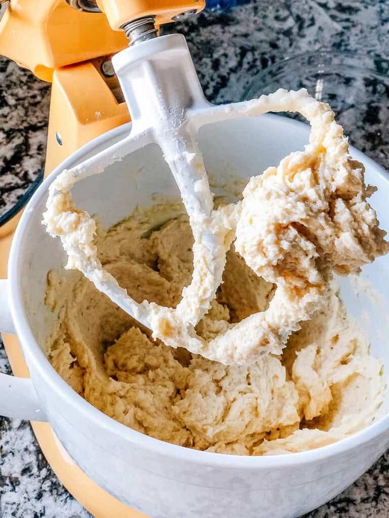 A close-up of buttery sugar cookie dough being mixed in a stand mixer, with specks of vanilla bean