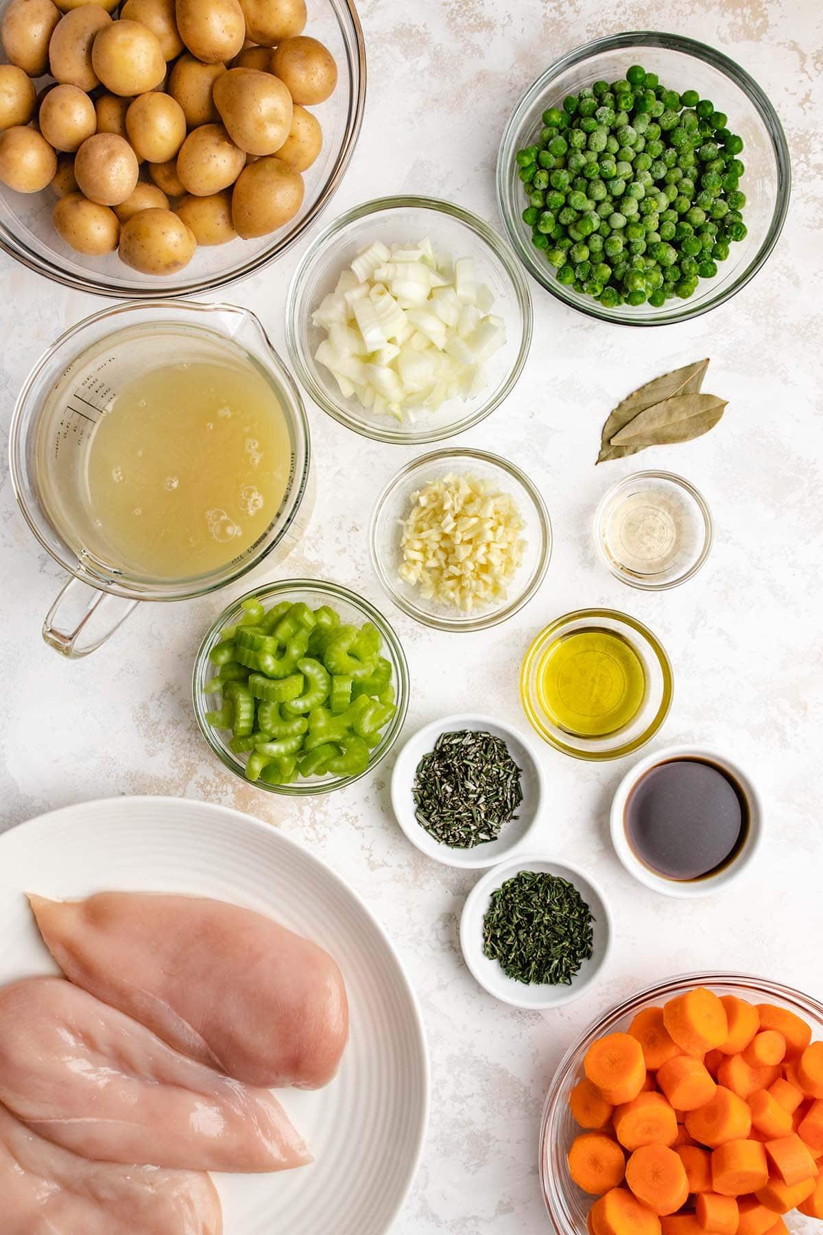 Ingredients laid out for chicken stew, featuring chicken, vegetables, herbs, and broth