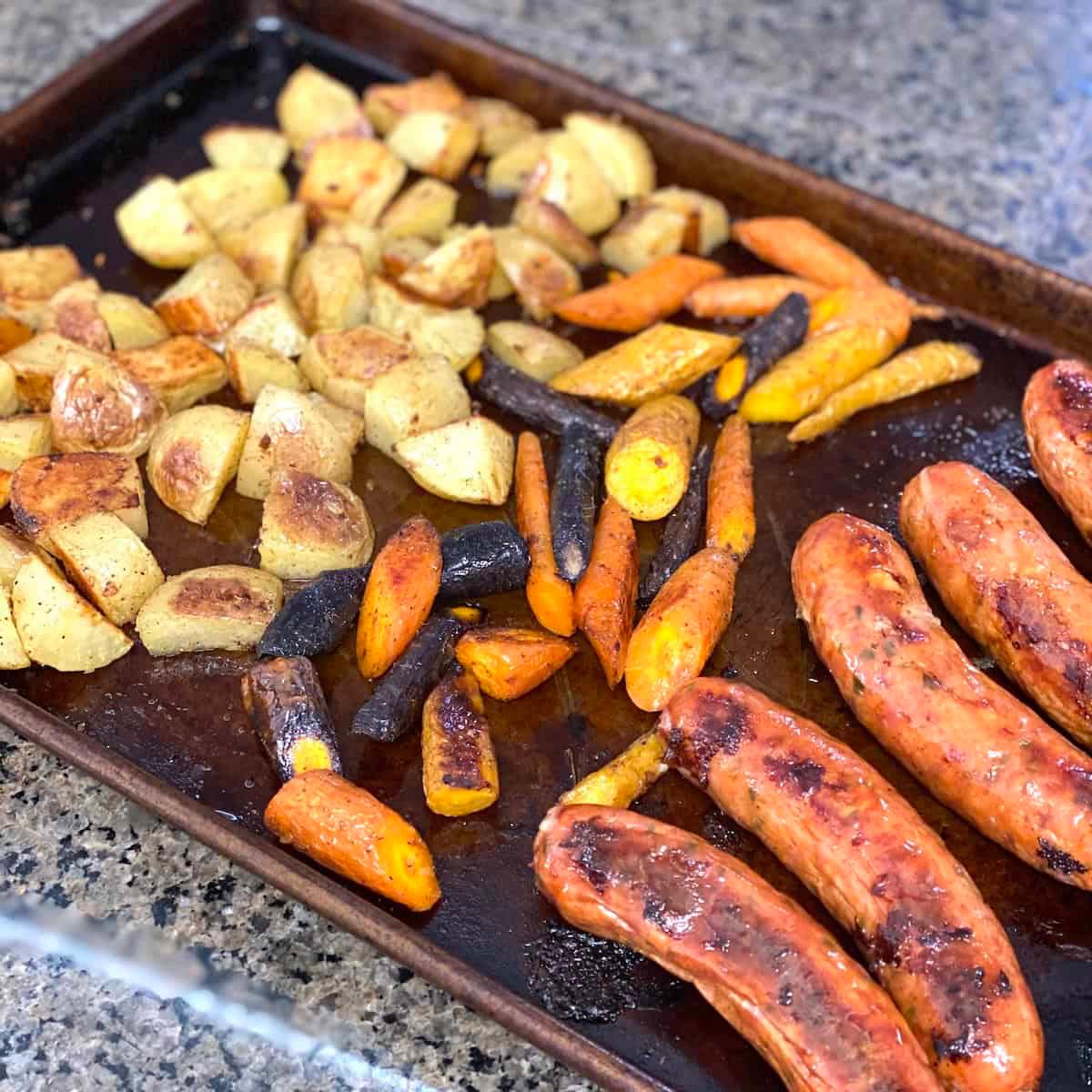hand placing colorful vegetables onto a baking sheet next to sausage links and raw eggs