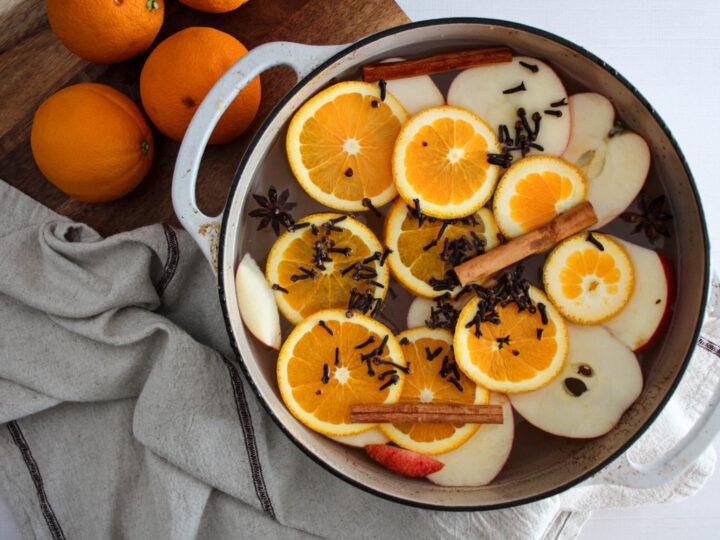 Close-up of whole cloves and orange zest being added to a simmering pot.
