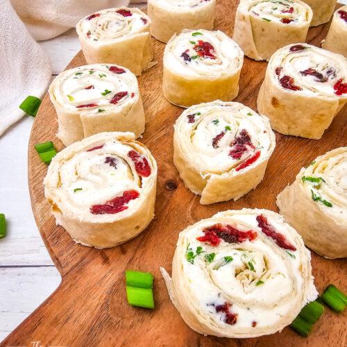 Hands assembling cranberry feta pinwheels on a cutting board, ready for slicing