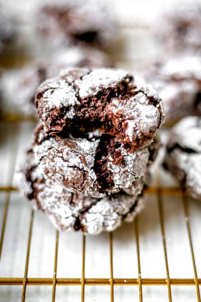 Child's hand reaching for a chocolate crinkle cookie on a cooling rack, slightly blurry background of a warm kitchen