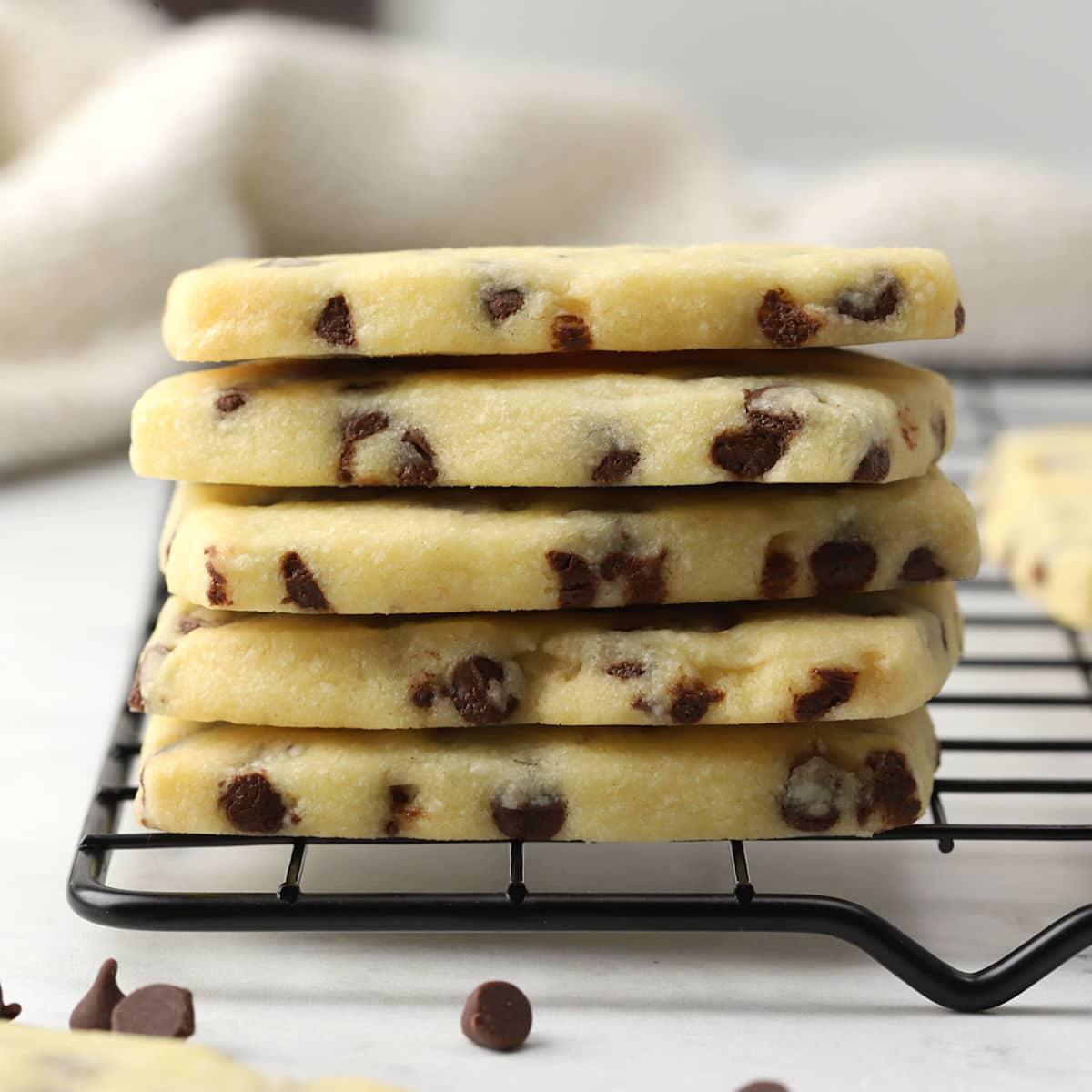A cooling rack filled with both plain and chocolate-dipped shortbread cookies, a tea cup in the background