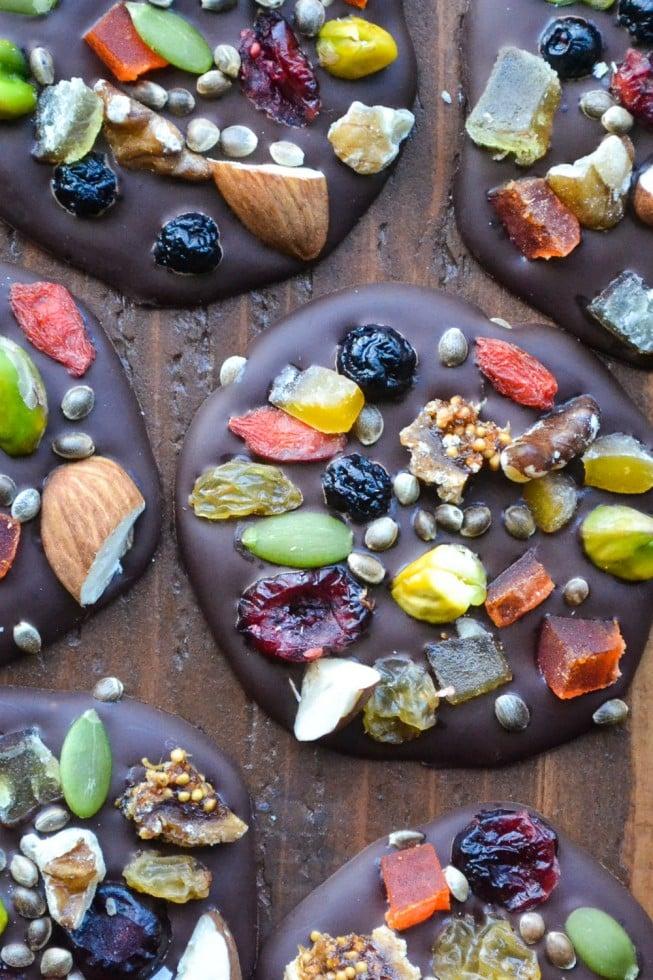 assortment of dark chocolate mendiants with various colorful toppings on a white platter