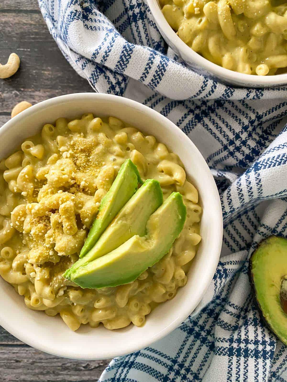 ingredients for guacamole mac on a wooden countertop, including avocados, pasta, cheese, and spices