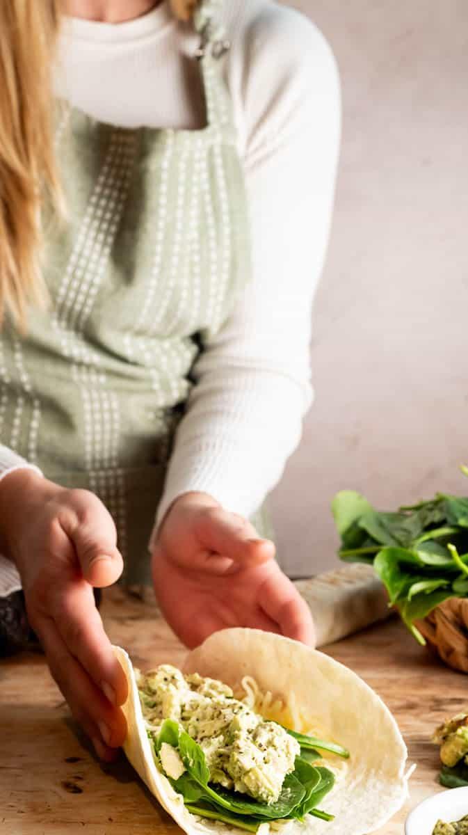 woman preparing creamy chicken spinach wraps in kitchen