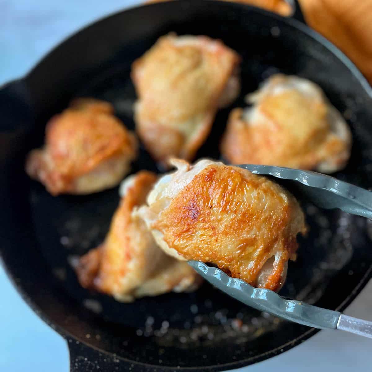 Close-up of golden-brown crispy chicken skin in a hot cast iron skillet