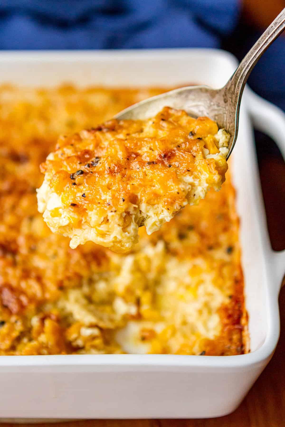 Serving spoon dishing out creamy baked corn casserole from a baking dish