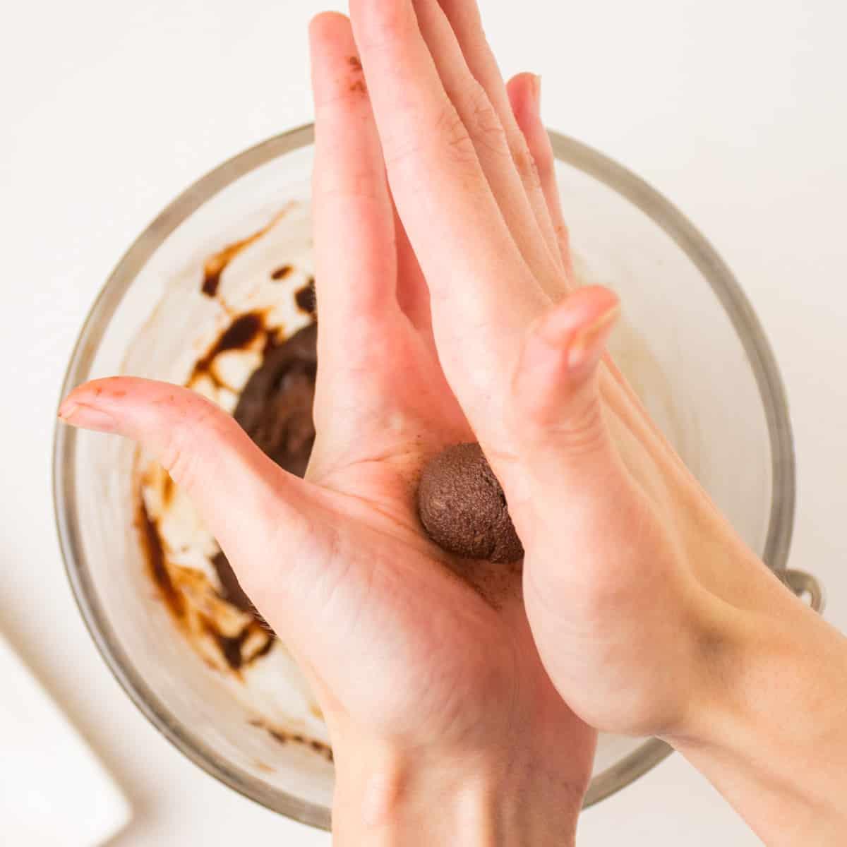 Person rolling espresso truffle mixture between their palms, close-up.