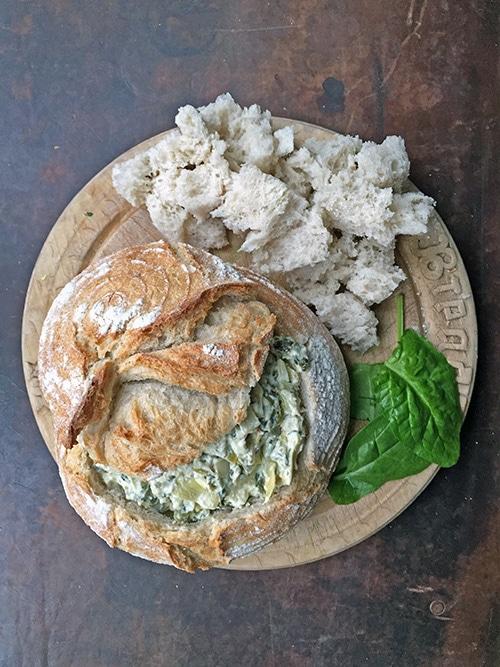 Close-up of bubbling, golden brown spinach artichoke dip in a rustic baking dish, with crusty bread for dipping