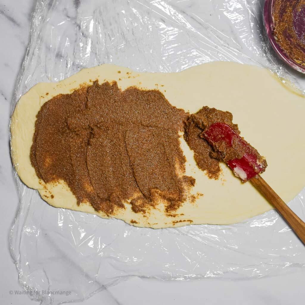 Overhead shot of cinnamon sugar filling being spread onto rolled out dough
