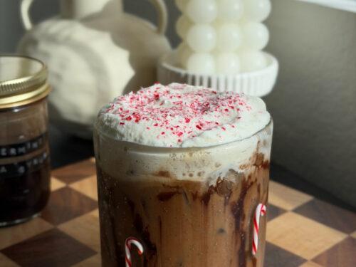 ingredients for peppermint mocha laid out on a kitchen counter: coffee beans, peppermint syrup, chocolate syrup, milk, and whipped cream