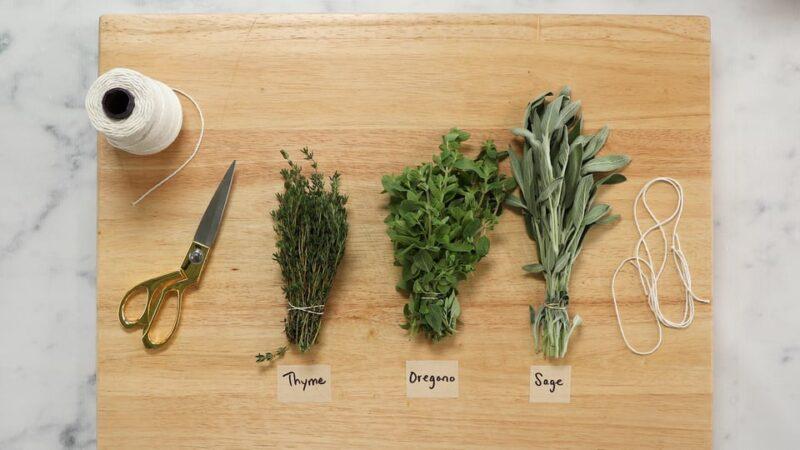 Close-up of fresh rosemary, thyme, and sage being chopped on a wooden board