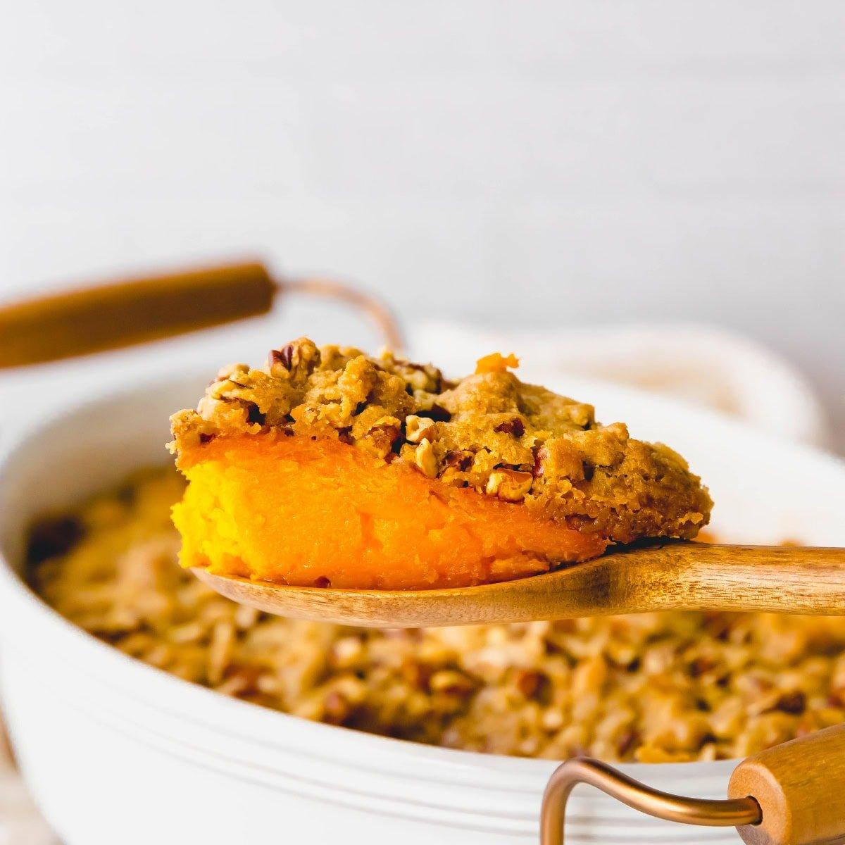 Hand scooping a serving of sweet potato casserole onto a plate