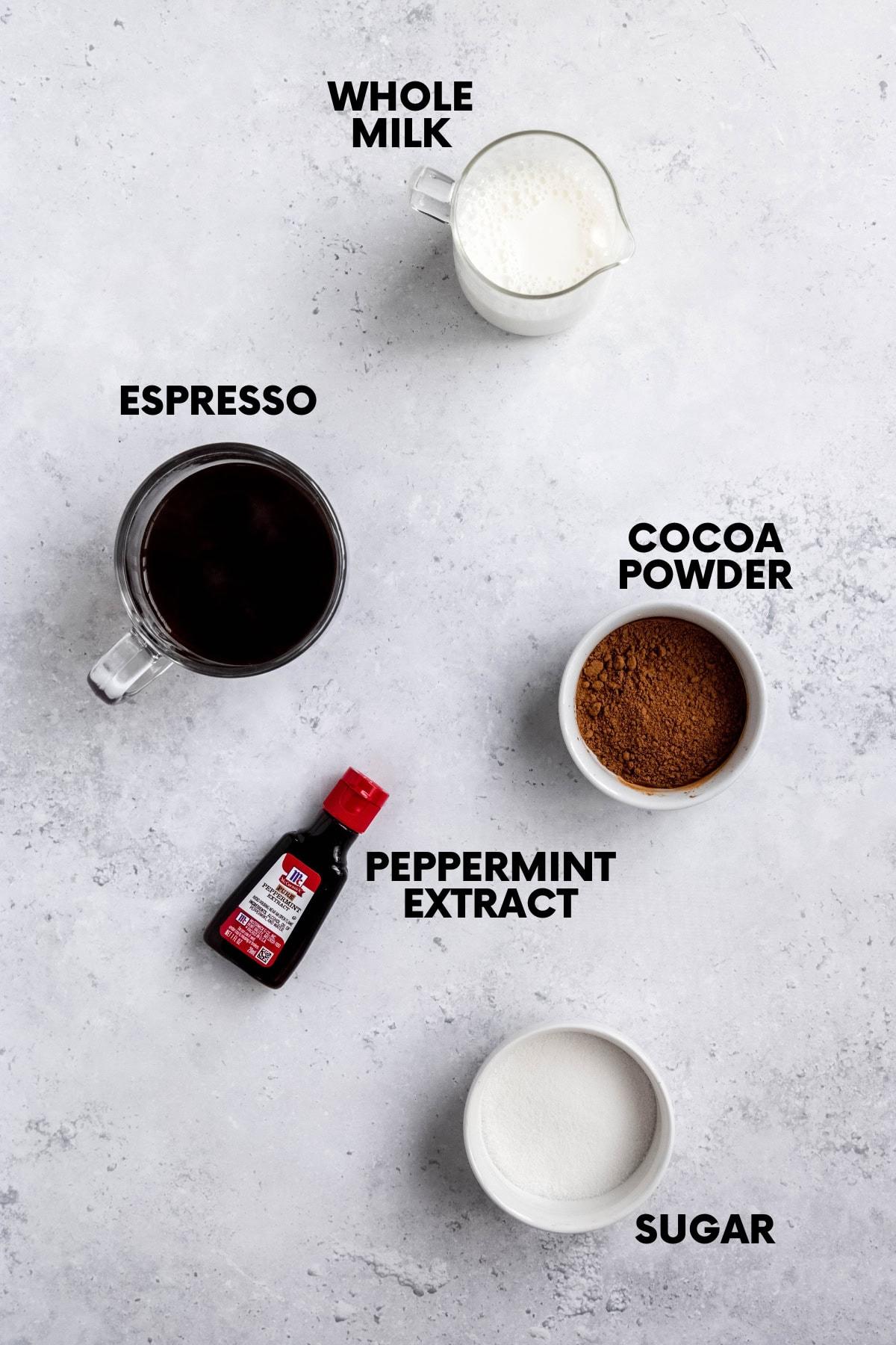 Overhead shot of ingredients for peppermint mocha on a wooden table, including coffee, chocolate syrup, milk, and peppermint extract