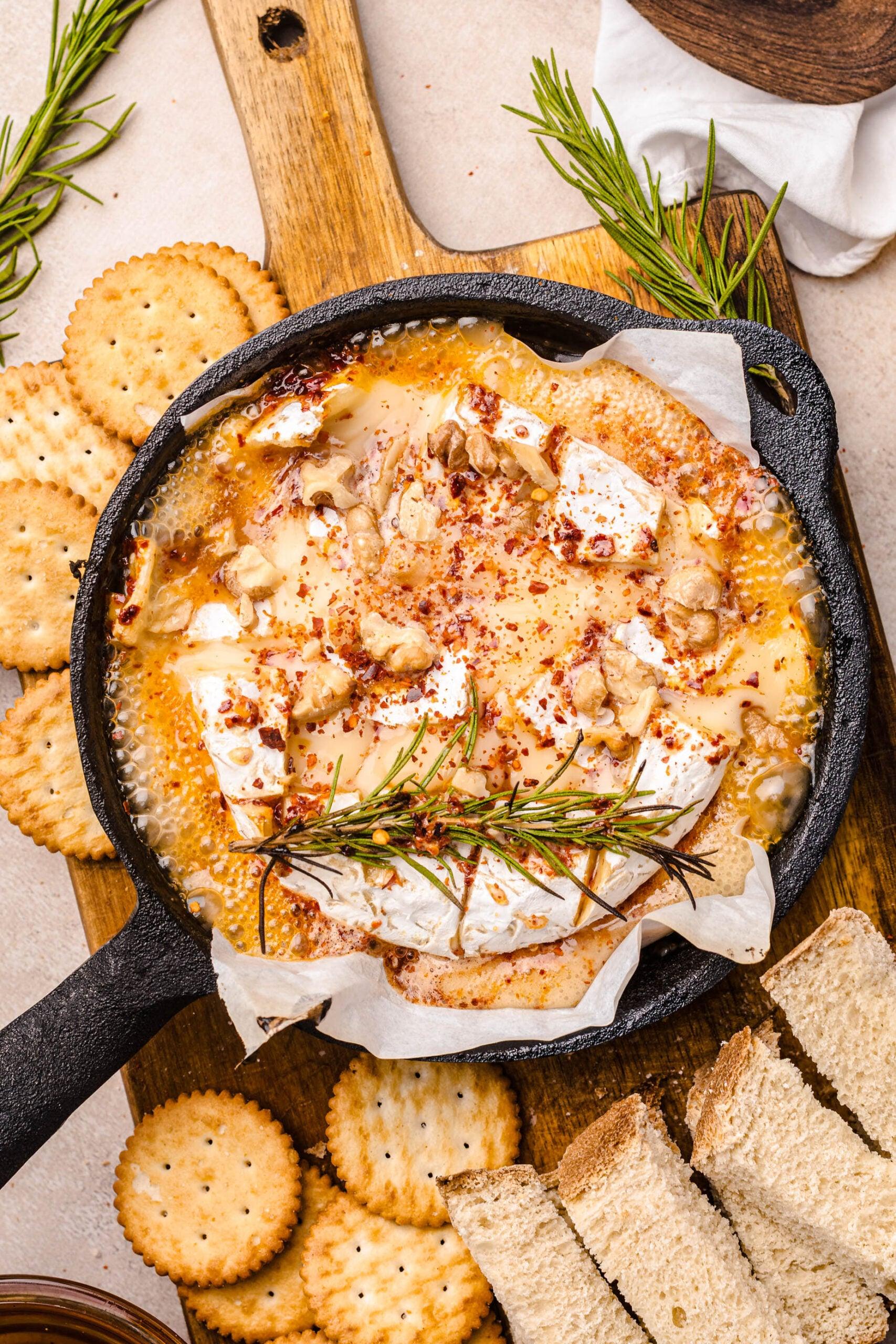 Warm baked camembert cheese wheel with rosemary and honey drizzle, ready for a charcuterie board