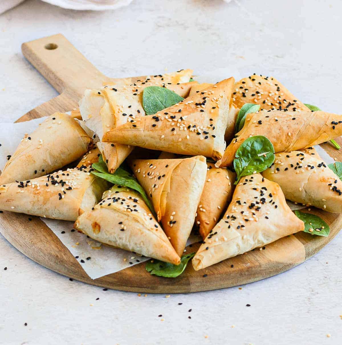 Various stages of spinach feta pastry triangle assembly on a wooden board